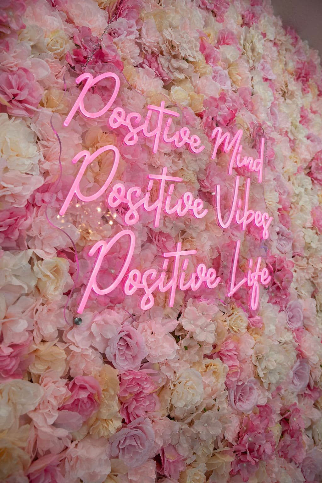A pink neon sign reading Positive Mind, Positive Vibes, Positive Life on the flower wall