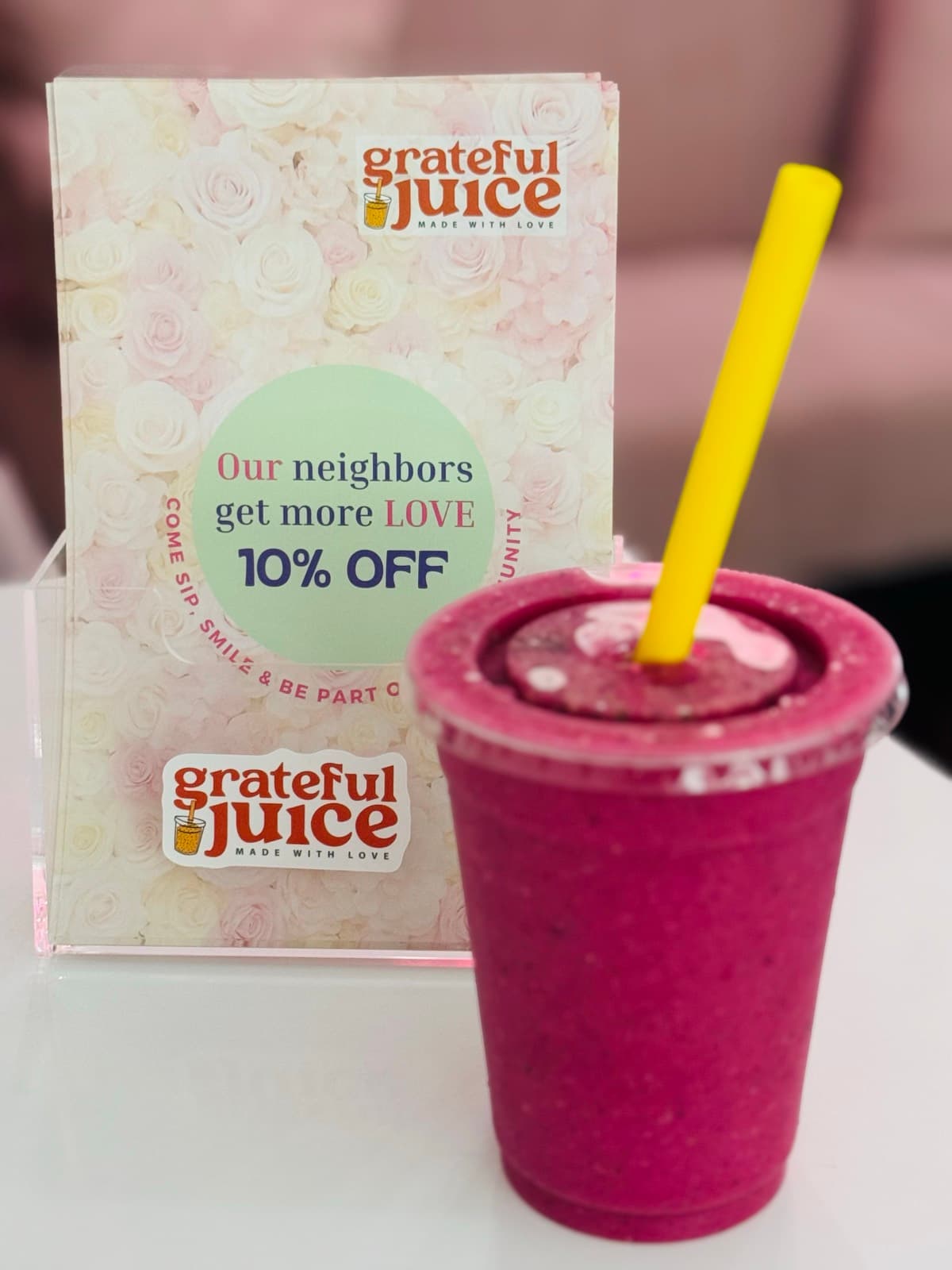 A deep pink berry smoothie beside a Grateful Juice card on the counter