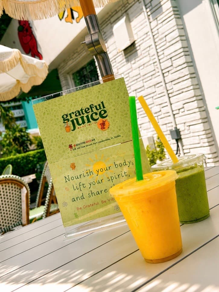 A mango smoothie and a green smoothie on the patio table under a fringed umbrella