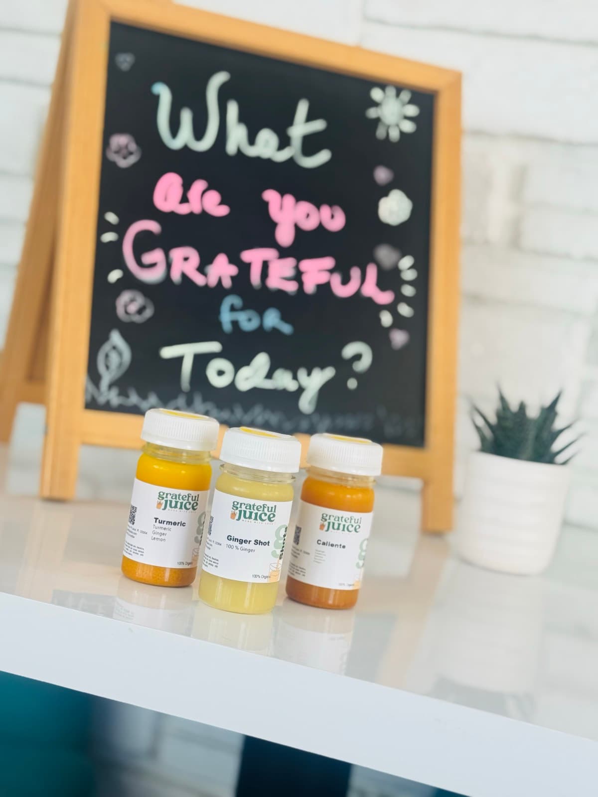 Turmeric, ginger and caliente wellness shots in front of a chalkboard asking what are you grateful for today