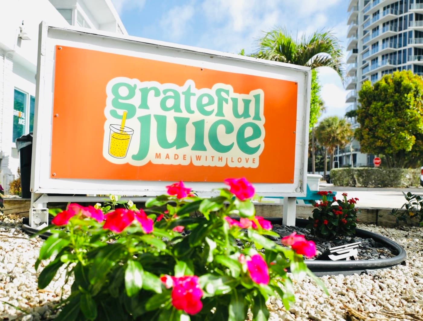 The orange Grateful Juice sign surrounded by pink flowers
